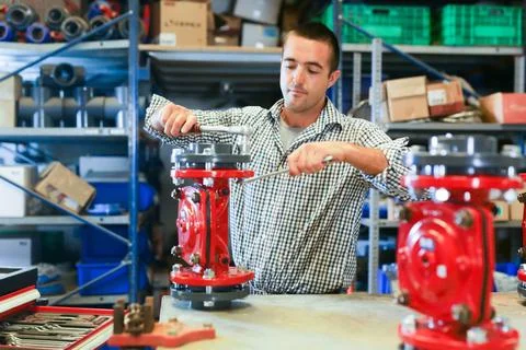 Factory worker assembles shutoff valves using various tools indoor Stock Photos