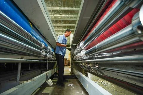 Factory Worker Bending Down to Inspect Large Printing Machinery Stock Photos