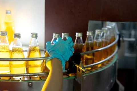 Factory worker hand checking glass bottles with yellow liquid fruit juice b.. Stock Photos