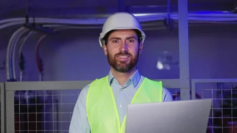 Factory worker in hard hat, green vest using laptop, serious electrician at work 動画素材 256230720