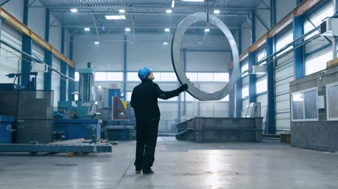Factory worker in a hard hat is moving a metal detail with a remote crane Stock Footage 61882493