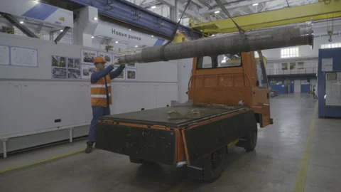 Factory worker in a hard hat is moving a metal detail with a remote crane Stock Footage 103354857
