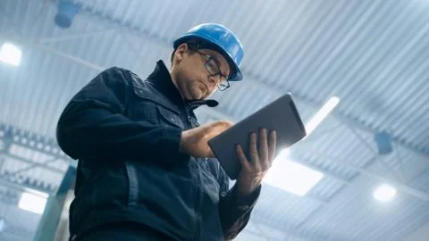 Factory worker in a hard hat is using a tablet computer. Foto stock