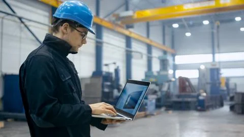 Factory worker in a hard hat is using a laptop computer with an engineering s Stock Photos