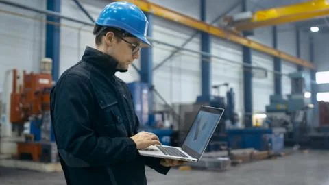Factory worker in a hard hat is using a laptop computer with an engineering s Foto stock