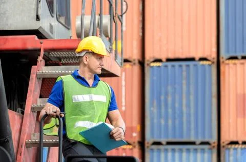 Factory worker man in hard hat and safety vest standing on container stackers 写真素材