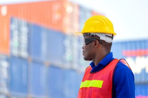 Factory worker man in hardhat and safety vest standing at containers cargo Stockfoto's