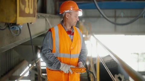 Factory worker in orange safety gear controlling cathead in workshop Video stock 272756210