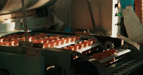 A factory worker places waffle cones on a conveyor belt for further ice cream Stock Footage 255187811