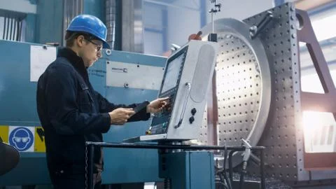 Factory worker is programming a CNC milling machine with a tablet computer. Stock Photos