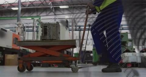 Factory worker pumping lever, guiding scissor-lift cart to lift and position Stock Footage 331085390