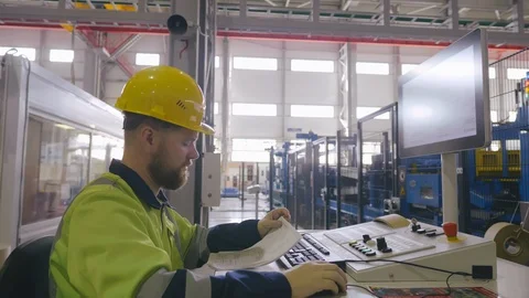Factory worker in uniform and hard hat looks to blueprints for programming a CNC 動画素材 119034452