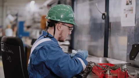 A factory worker wearing a hard hat, gloves, and goggles is cleaning parts. Stock Footage 316162253