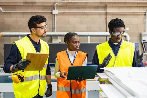 Factory workers collaborating in a busy lumberyard discussing project details Foto stock