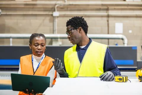 Factory workers collaborating on project using laptop Stock Photos