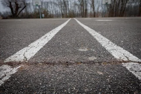 Faded white lines stretch across a weathered asphalt court, leading towards d Stock Photos