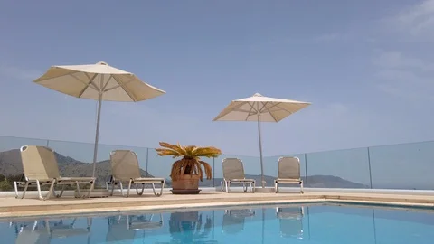 Fading Out Tilt Shot of Sun Loungers &amp; Umbrellas Adjacent to Luxury Pool Vidéo 109616492