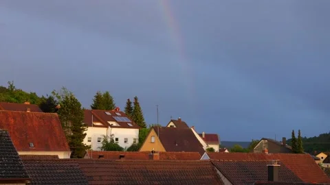 Fading rainbow in the sky over rural village Otterbach, old tiled roofs, trees 库存影片 131404510