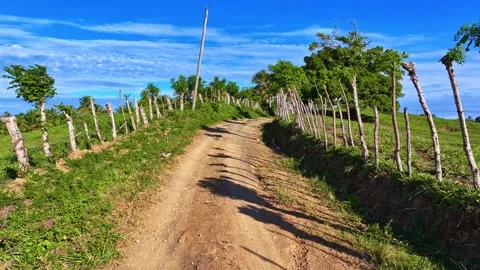 Faint clouds hovering over a dirt road amid tree-covered mountain hills. Видео 329964332