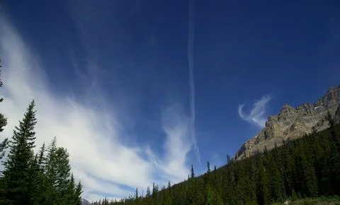 Faint Condensation Trail Cuts Through Delicate Cirrus Clouds and Blue Skies Stock Photos