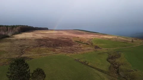 Faint rainbow arching over moorland and forestry under brooding grey sky Stock Footage 341315692