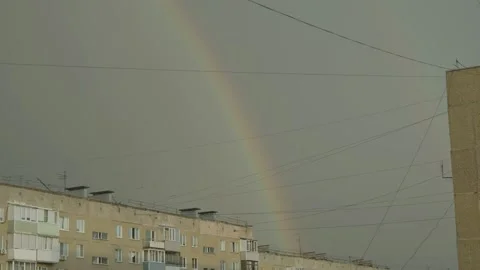 A faint rainbow arcs across a dark gloomy sky over residential building Stock Footage 336559579