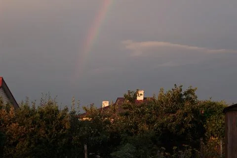 Faint Rainbow in Dark Sunset Sky over Countryside Village Roofs Fotos Stock