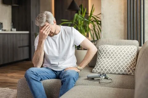 Fair-haired, bearded guy checking blood pressure at home, using tonometer w.. Stock Photos