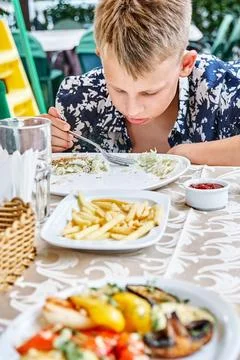 Fair-haired boy eats lunch at hotel restaurant on holiday Stock Photos