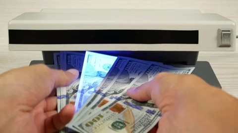 A fake banknote shines between real banknotes under the light of detector. Stock Footage 79034955