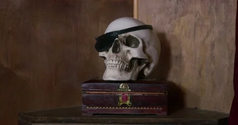 Fake or real human skull with a pirate eye patch stands on a wooden box on Stock Footage 197343355