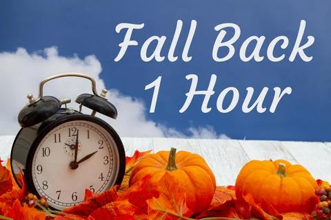 Fall Back 1 hour message with fall leaves, alarm clock, and pumpkins with sky Stock Photos