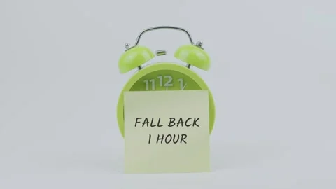 Fall Back 1 Hour word on sticky note in front of green clock and ringing Stock Footage 313982992