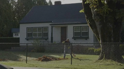Fall clean-up. A man cleaning up leaves in front of his house. Видео 118265832