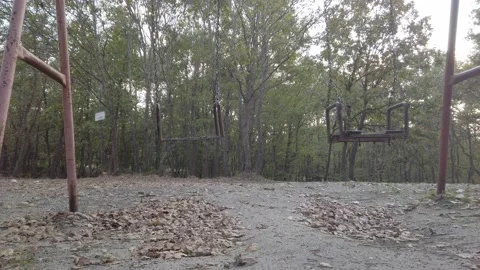 Fall dark forest, playground in clearing. Old rusty metal swing swaying in wind Stock Footage 142393196