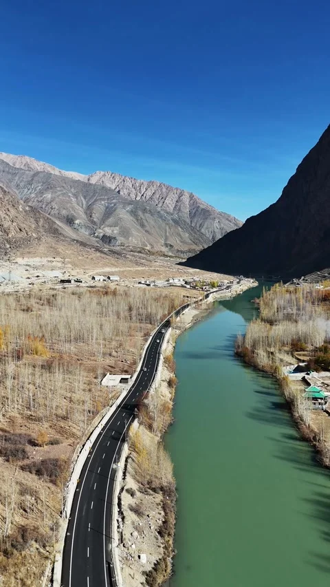 Fall-hued forest lining road and river in vertical drone aerial footage. Stock Footage 310662269