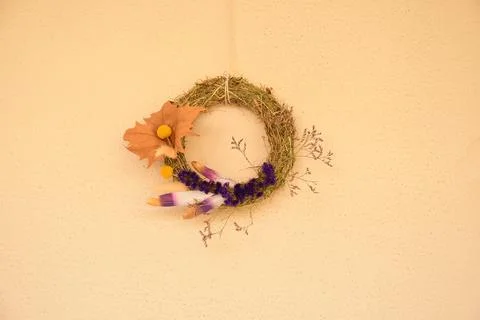 Fall wreath made of dried grass and herbs hangs on textured wall background w Stock Photos