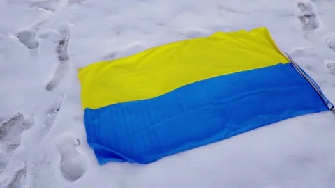 Fallen defeated Ukrainian flag in snow laying on the ground symbolic of war with Stock Footage 172201699