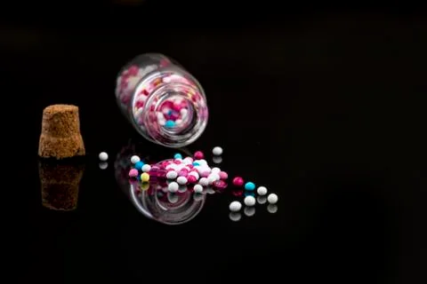 Fallen down glass bottle filled with sweet pearls on black background with re Stock-Fotos