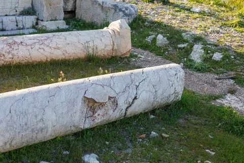 Fallen white marble columns lying on grassy ground at archaeological Stock Photos