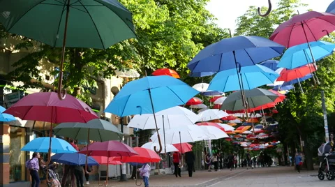 Falling art installation of suspended colored umbrellas  above walking street Stock Footage 63423383
