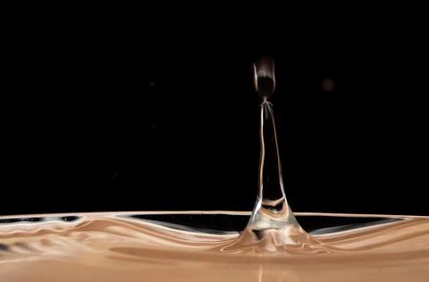 Falling brown drop on a black background . Stock Photos