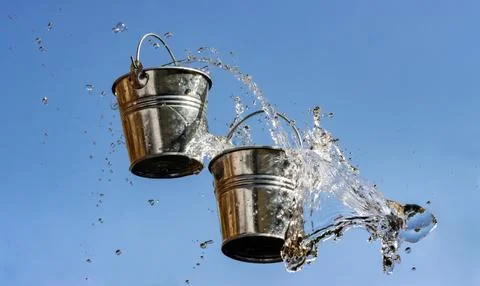 A falling buckets splashes water, on a background of blue sky. Stock Photos
