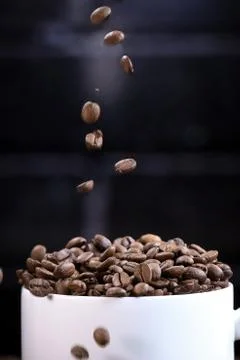 Falling coffee beans in a white mug against the background of a dark brick wall. Stock Photos