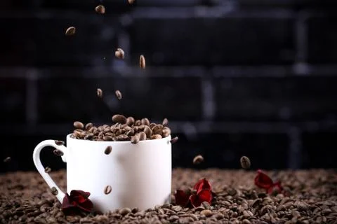 Falling coffee beans in a white mug against the background of a dark brick wall. Foto stock