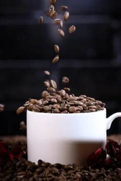 Falling coffee beans in a white mug against the background of a dark brick wall. Stock Photos
