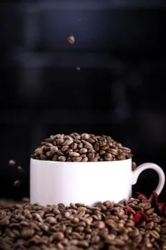 Falling coffee beans in a white mug against the background of a dark brick wall. Stock Photos