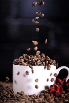 Falling coffee beans in a white mug against the background of a dark brick wall. Stock Photos