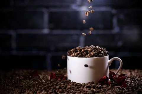 Falling coffee beans in a white mug against the background of a dark brick wall. Stock Photos