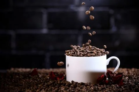 Falling coffee beans in a white mug against the background of a dark brick wall. Stock Photos